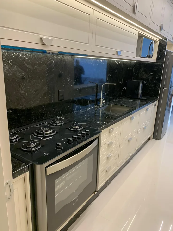 Bancada e painel de cozinha em pedra escura com veios, com recorte para cooktop